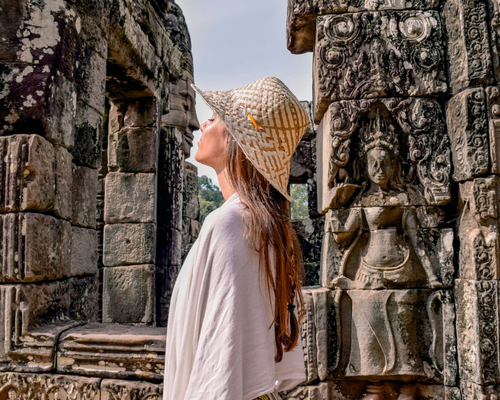 Woman in a straw hat admiring ancient stone carvings at Bayon Temple Angkor Wat