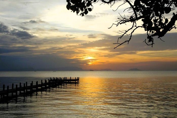 Golden sunset over the ocean with a wooden pier and silhouettes of islands in Kampot Cambodia