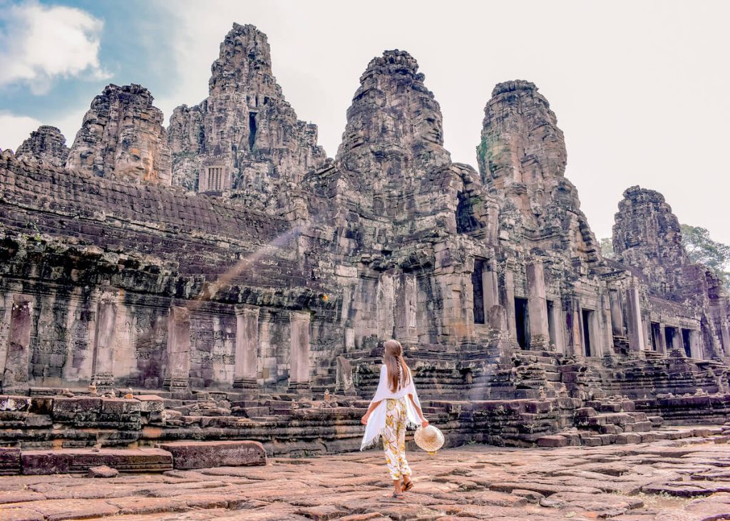 A traveler in a white dress at the ancient Bayon Temple face towers in Angkor Wat Siem Reap Cambodia