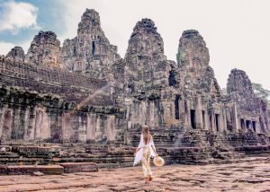 A traveler in a white dress at the ancient Bayon Temple face towers in Angkor Wat Siem Reap Cambodia