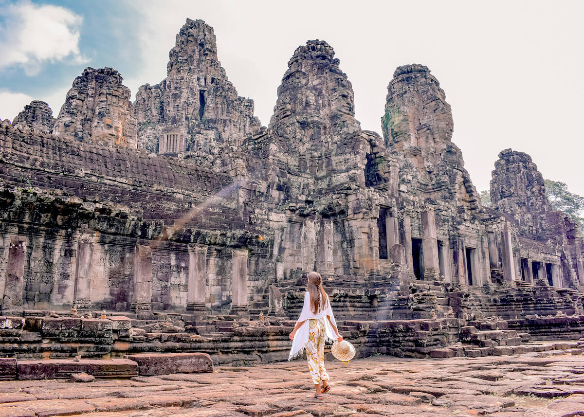 A traveler in a white dress at the ancient Bayon Temple face towers in Angkor Wat Siem Reap Cambodia