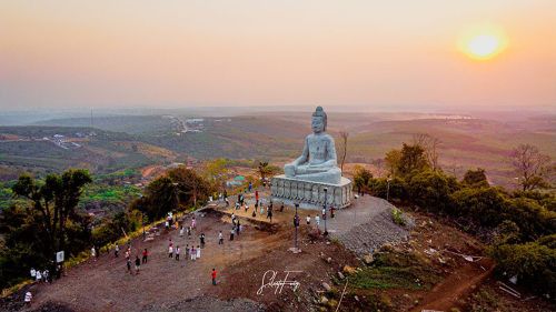 Giant white seated Buddha statue on a hilltop overlooking Banlung, Ratanakiri, Cambodia at sunset.