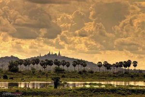 Scenic landscape view of the ancient stupas on Oudong Mountain with palm trees and lake at sunset